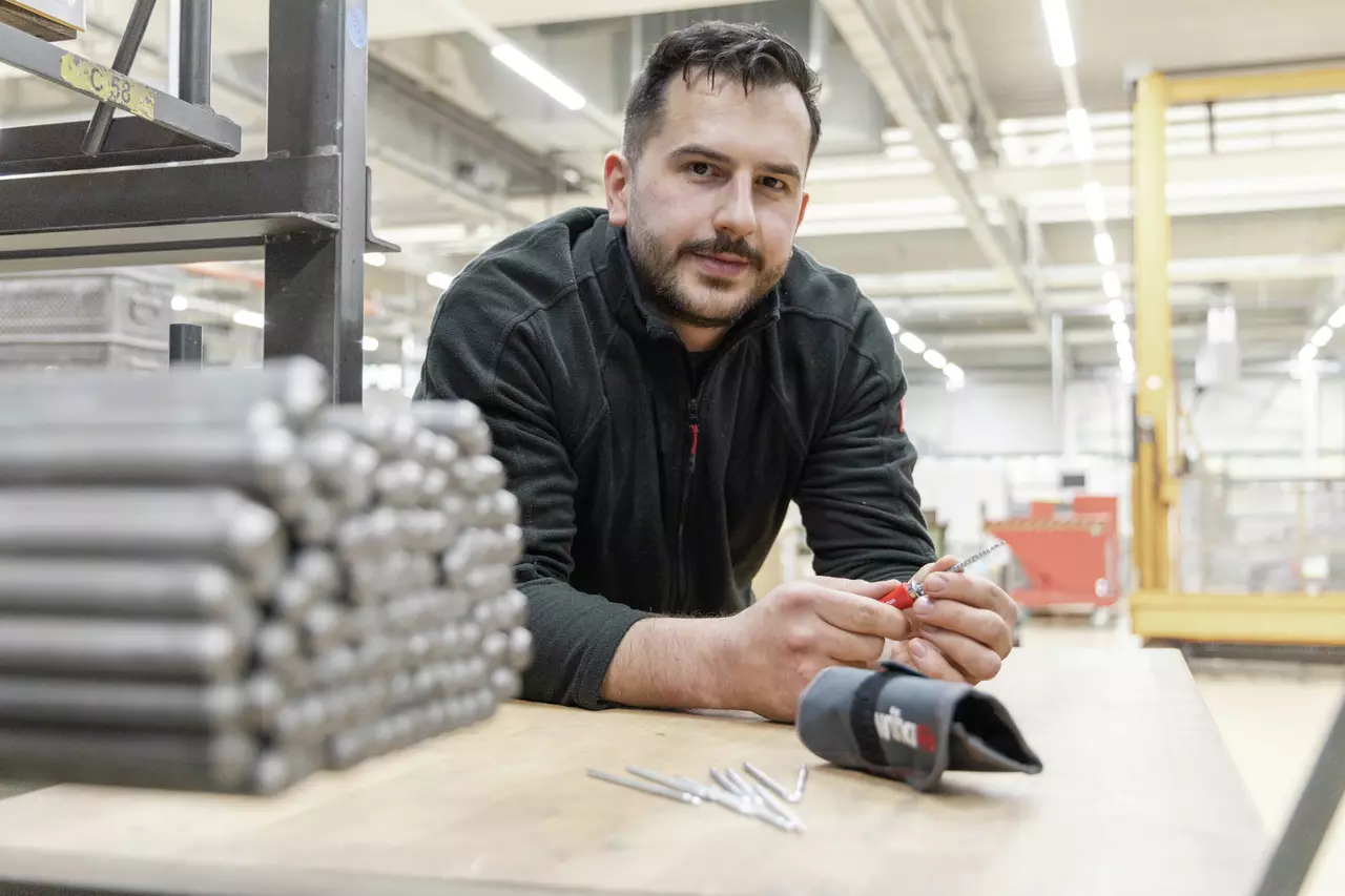 A person working in a workshop with a screwdriver and drill bits on a table.