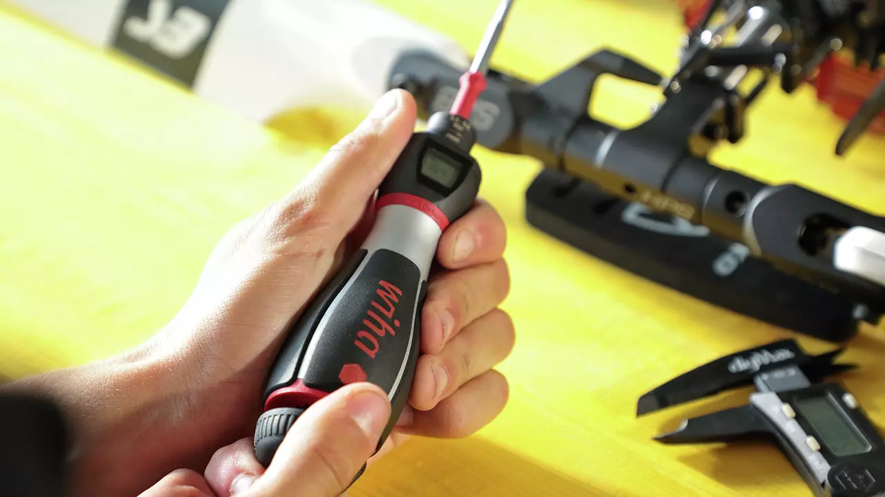 A person using a torque screwdriver on a mechanical part. The handle is black and red with a digital display.
