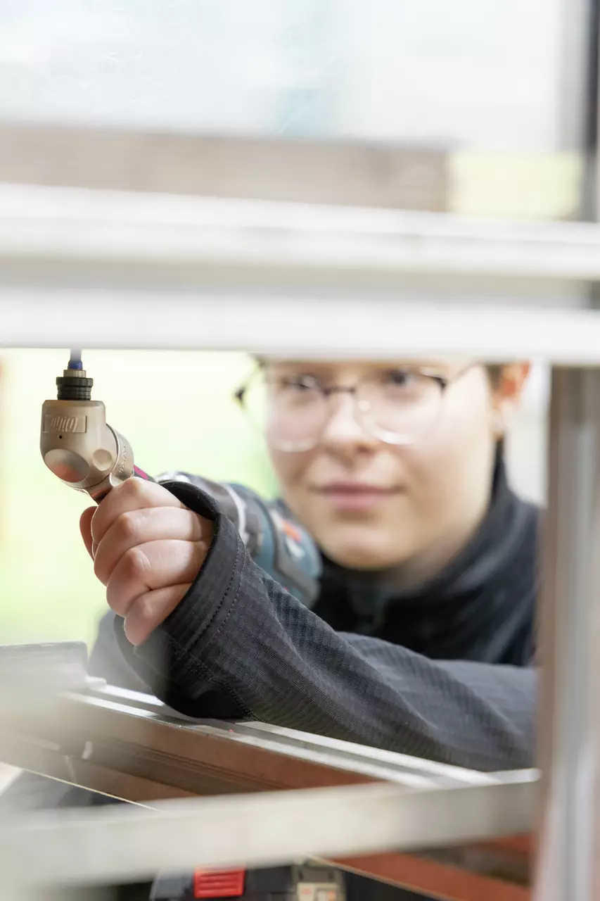 A person using a power tool with focus on the hand and tool, partially visible face in the background.