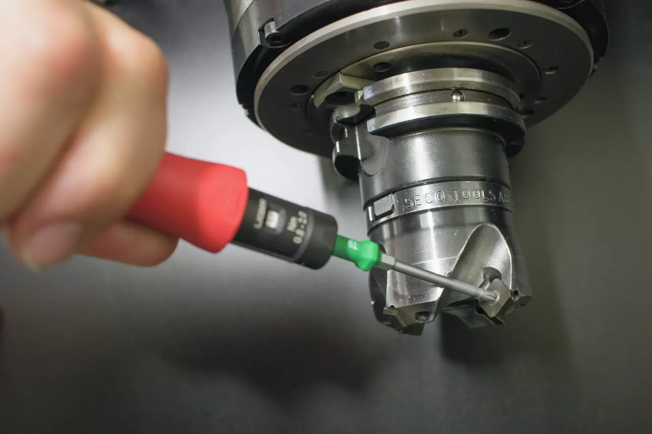 A hand uses a torque screwdriver on a metal cutting tool, adjusting a component.