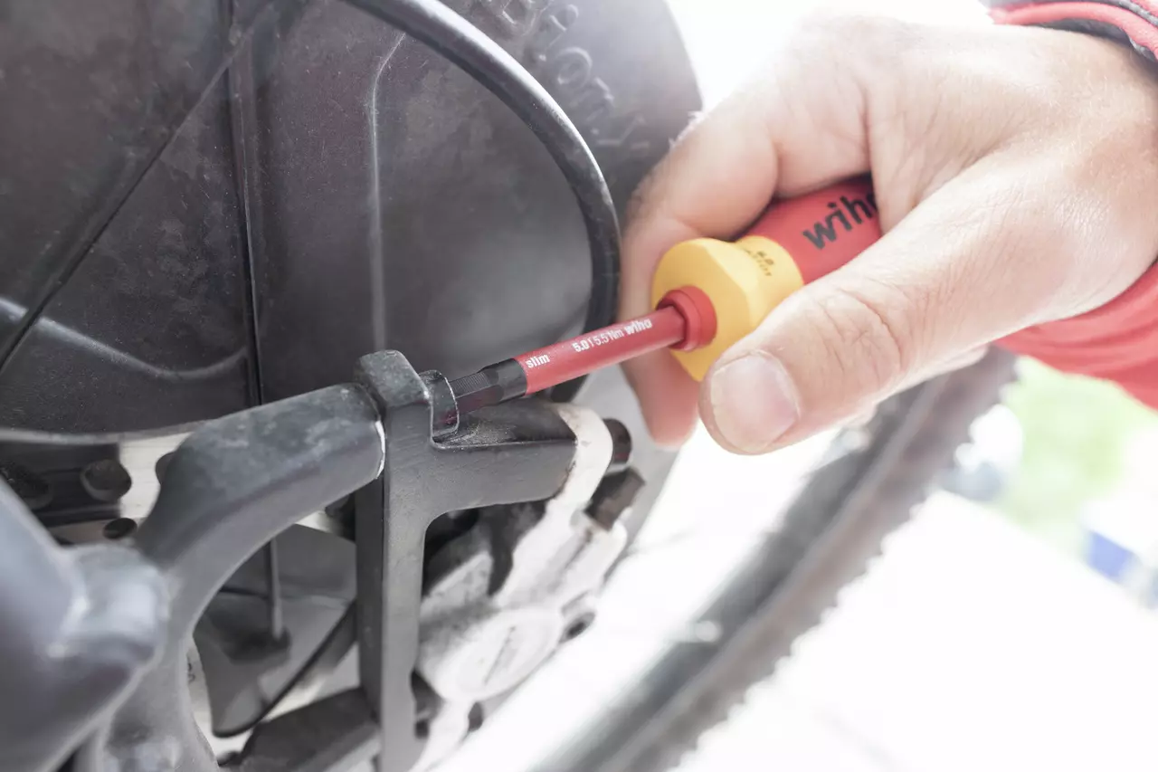A person uses an electric screwdriver on a bicycle component.