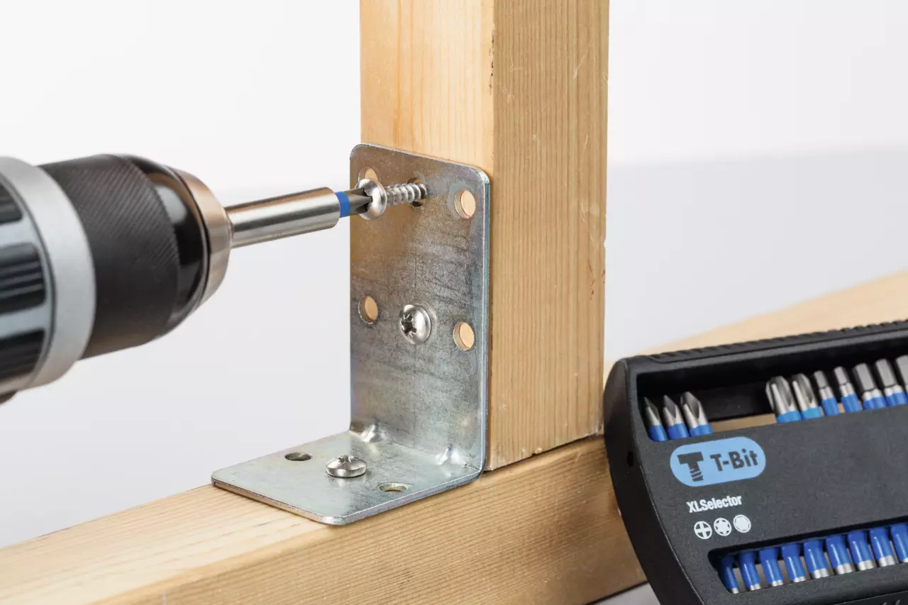 Power drill driving screw into metal bracket on wooden beams, with a bit set visible.