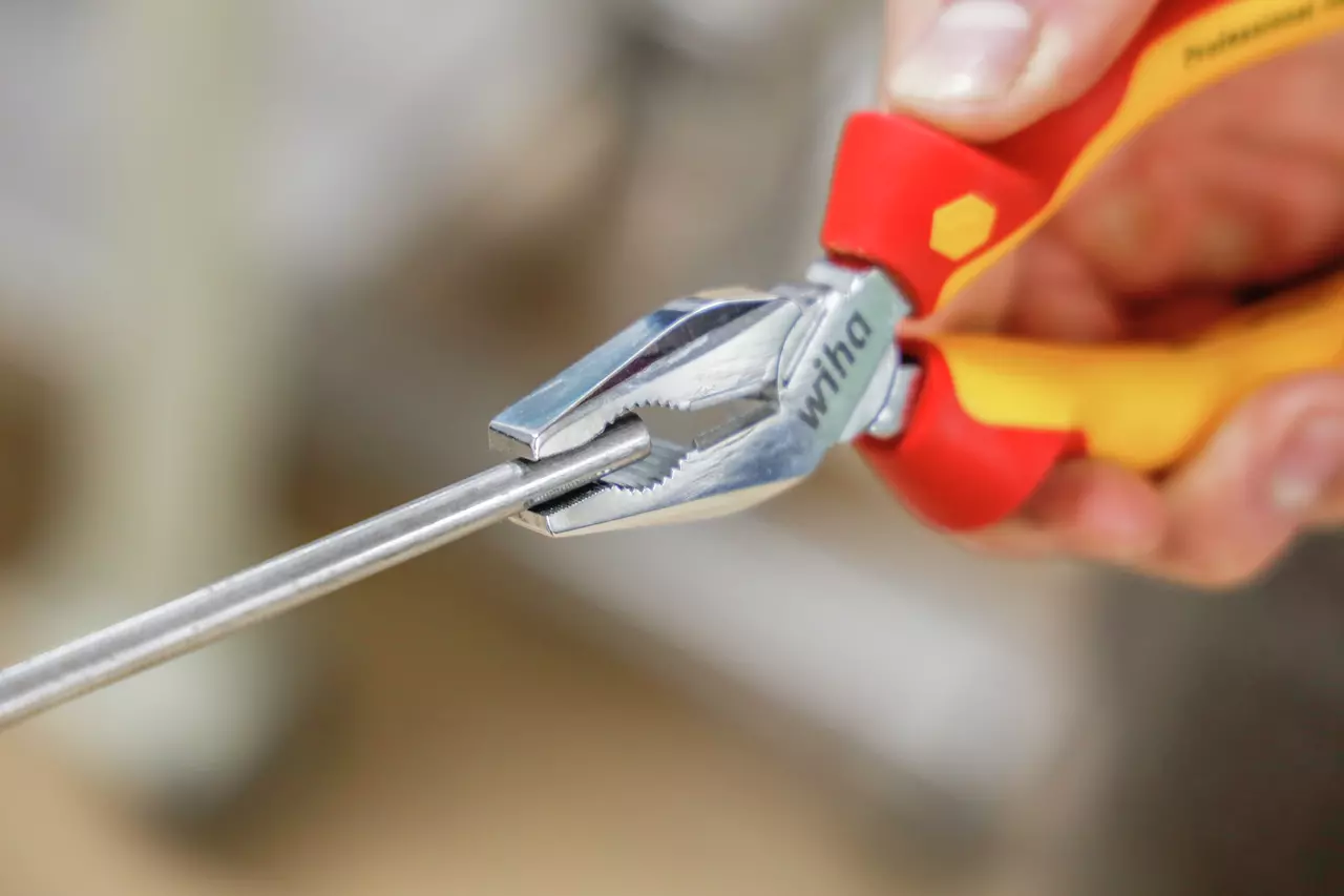 A person uses red and yellow pliers to grip a metal rod.
