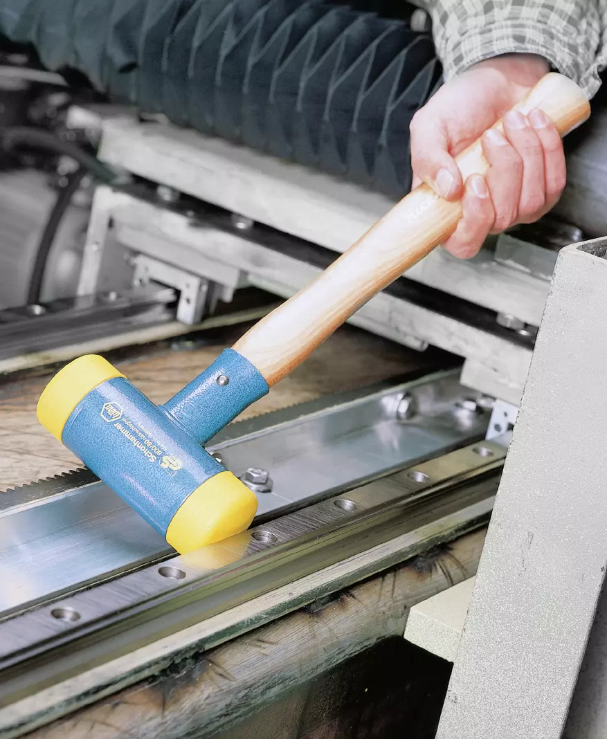 A person using a non-rebound mallet with a wooden handle and yellow rubber ends on a metal surface.