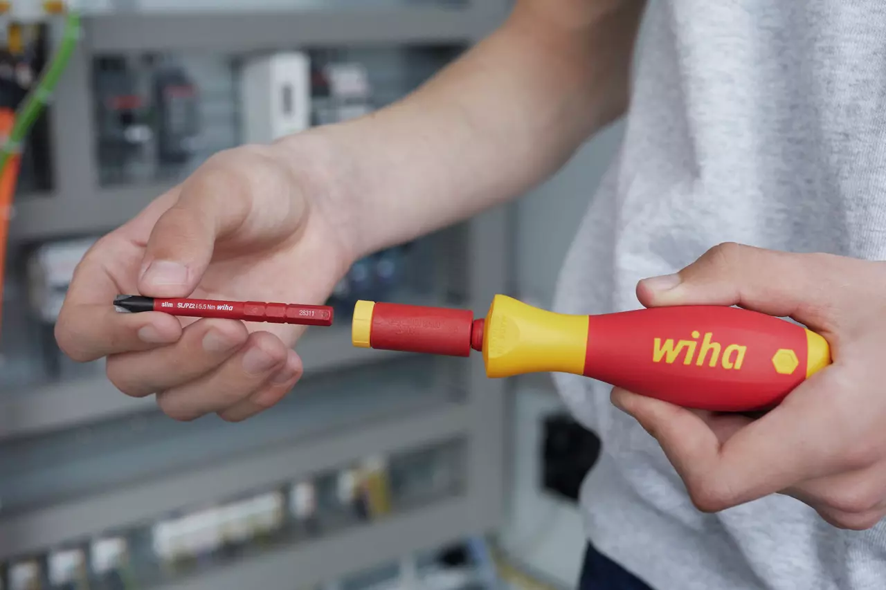 Person holding a red and yellow electric screwdriver with a detachable bit.
