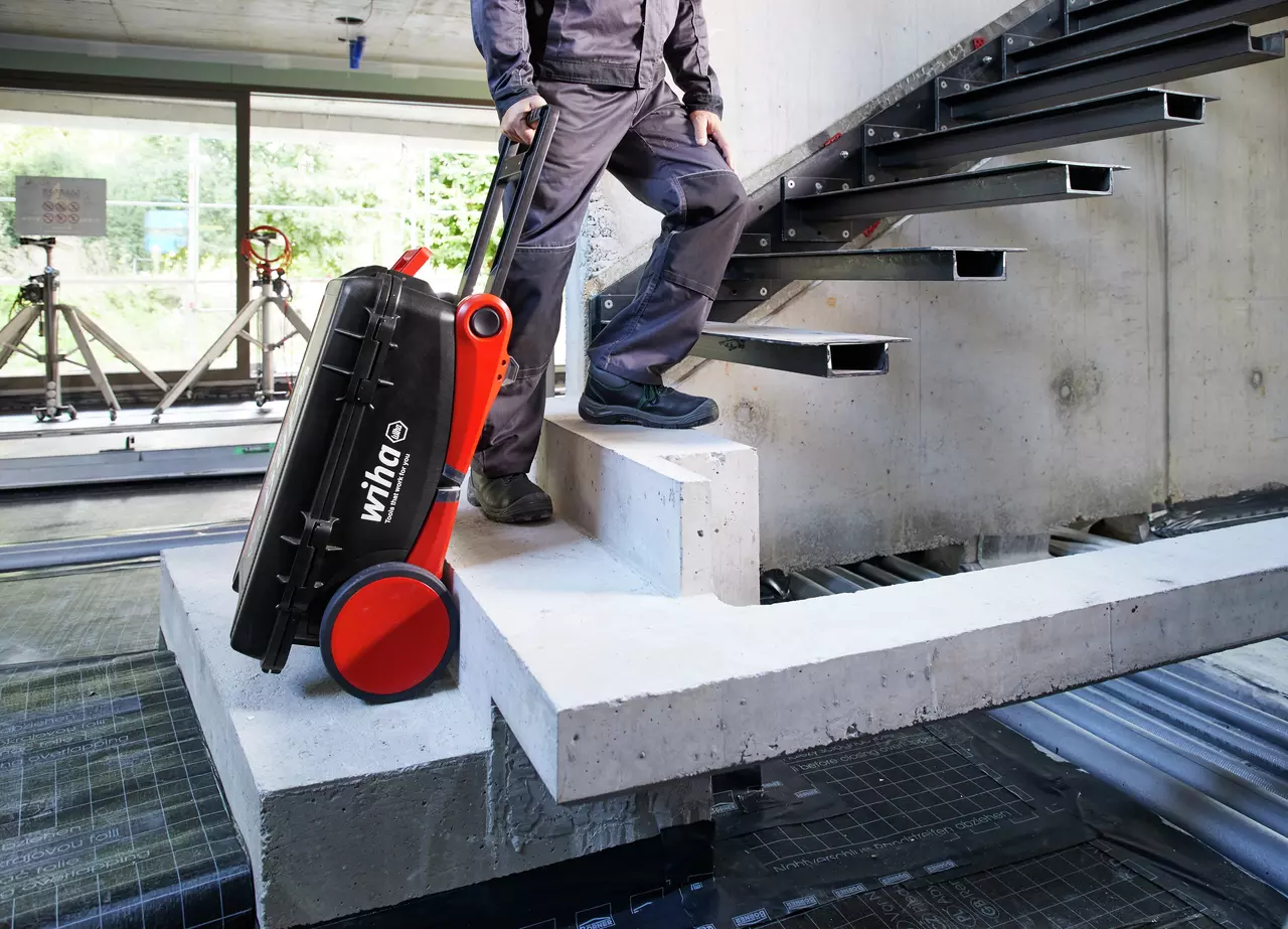 Person pulling a black tool case with red wheels up a concrete staircase.