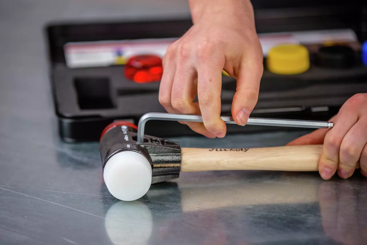 A person adjusts a mallet with a hex key on a metal surface.