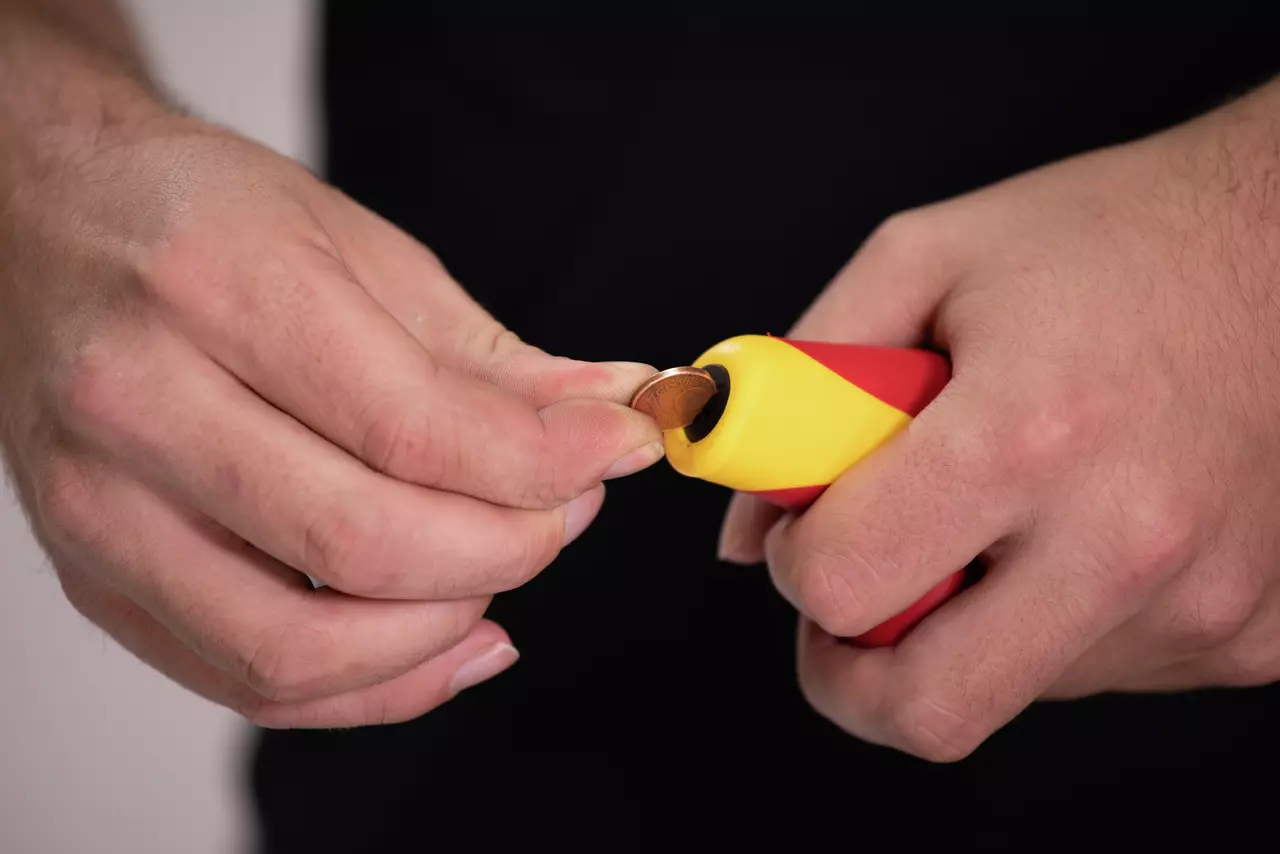 Person using a yellow and red tool to hold a small coin.