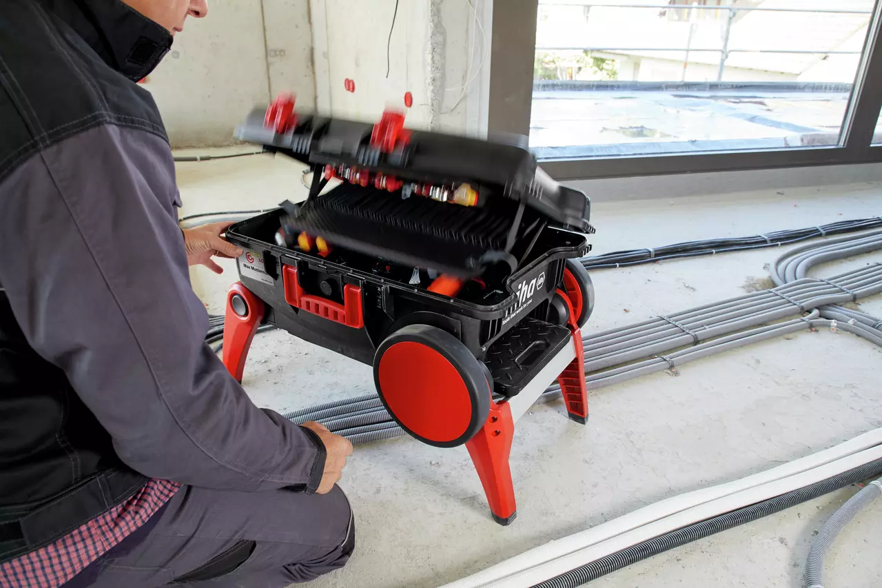 Person opening a black and red tool case on wheels in a construction setting.