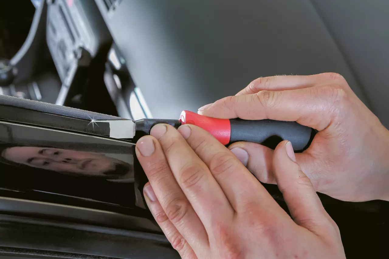A person using a red and black handled scraper on a car surface.