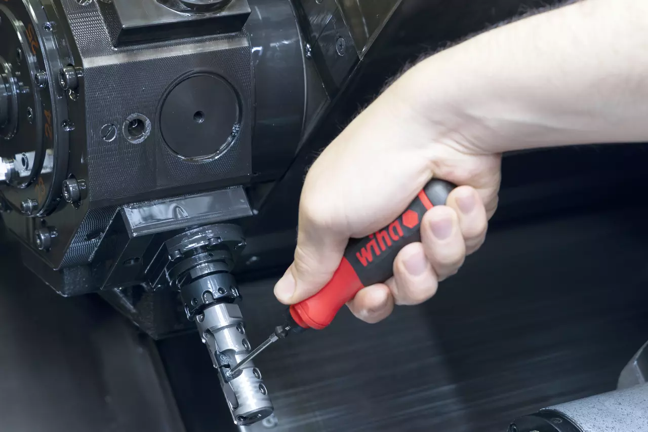 Hand using a red and black screwdriver on CNC machine