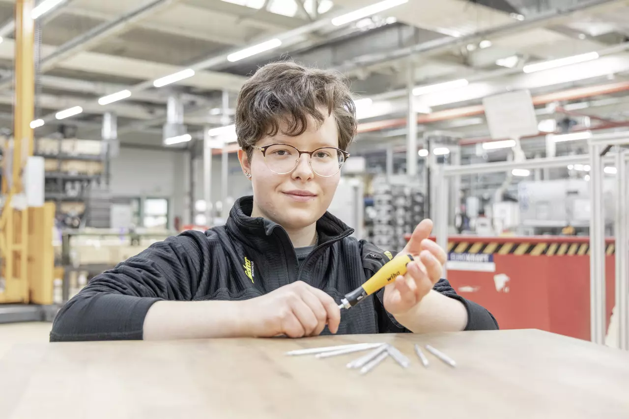Person with glasses holding a yellow screwdriver in a workshop, screwdriver bits on the table.