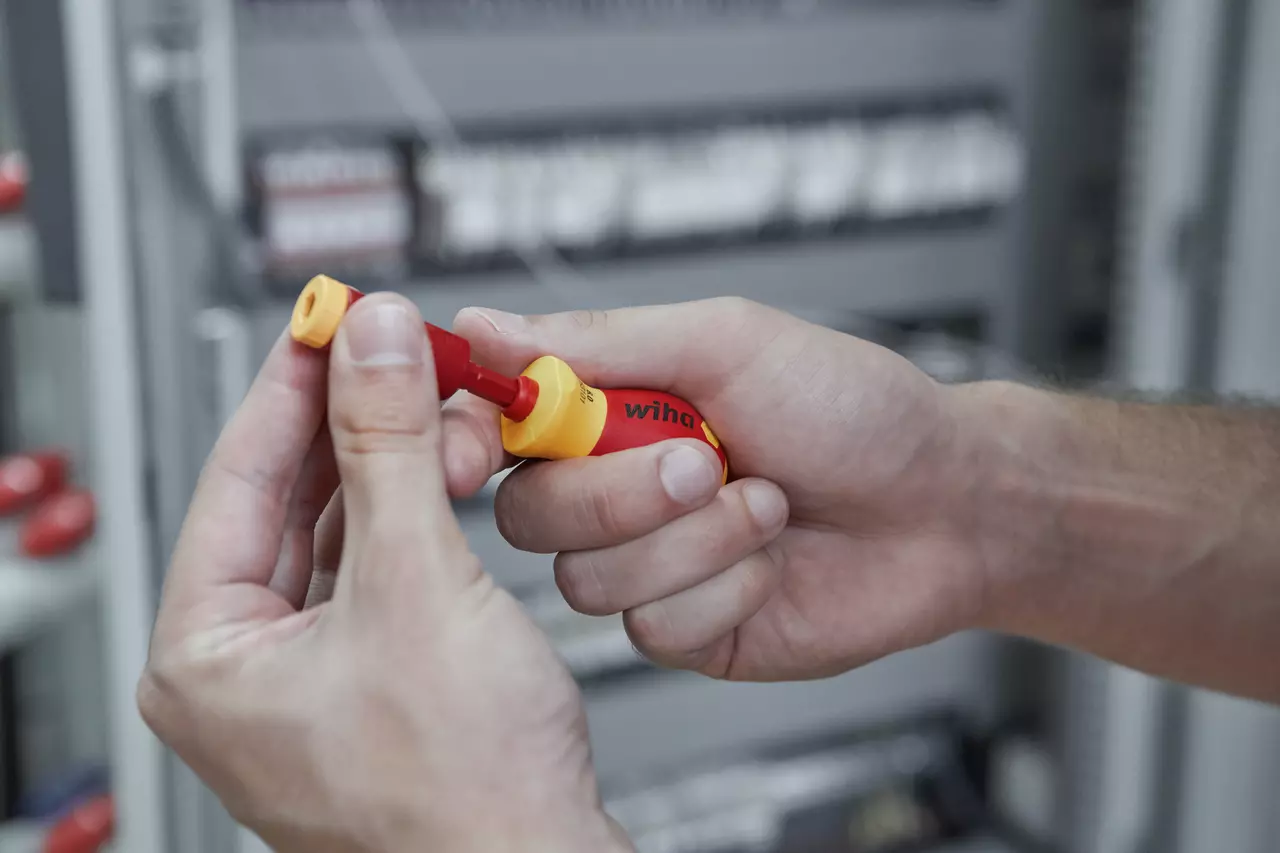 Person holding a red and yellow electric screwdriver with adapter in an industrial setting.