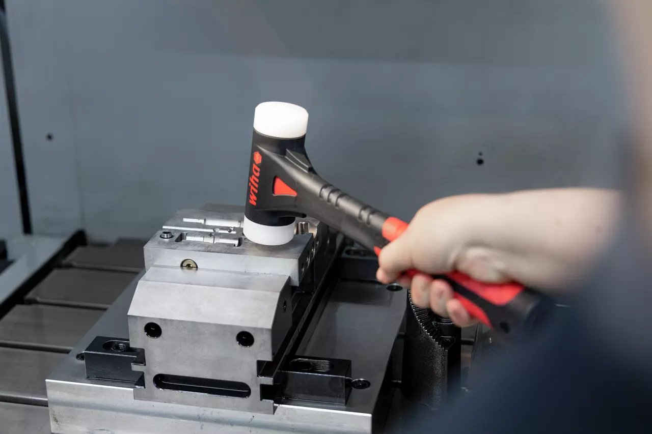 Eine Person benutzt einen Schonhammer mit weißem Kopf auf einem Metallwerkstück.