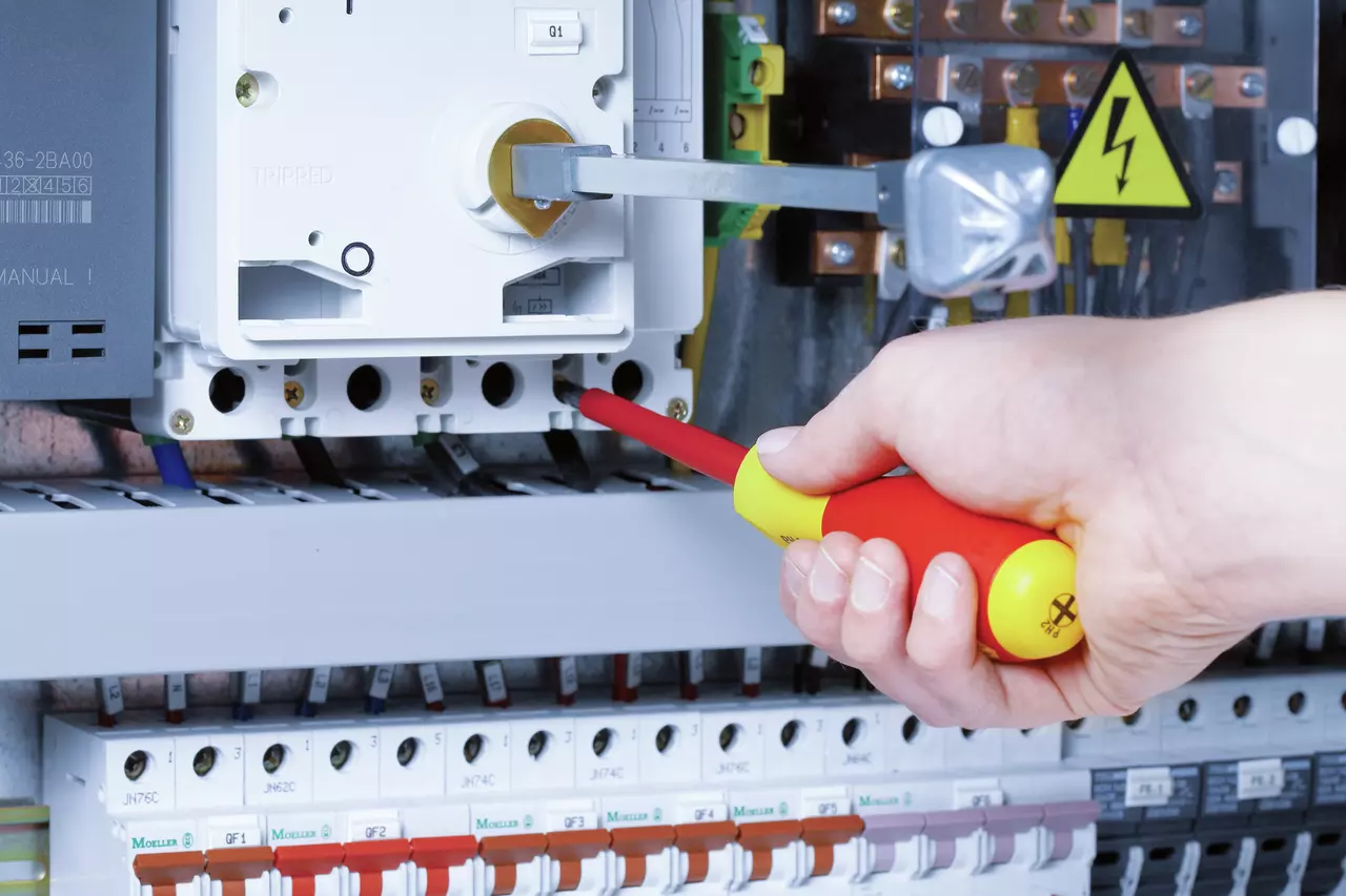 Hand using an insulated screwdriver on an electrical panel