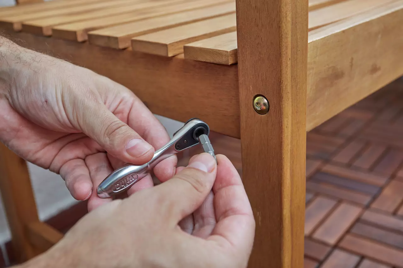 Person using a ratchet wrench to tighten a bolt on a wooden chair.