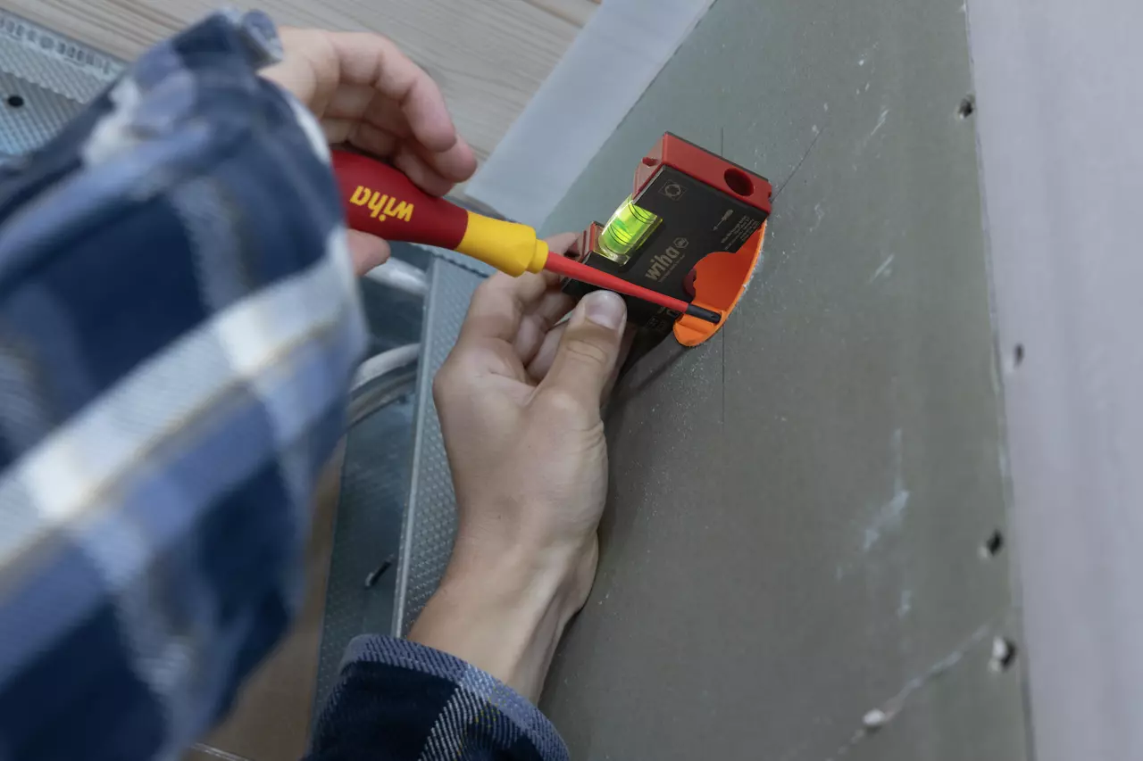 Person using a pocket level and screwdriver to adjust a wall socket.