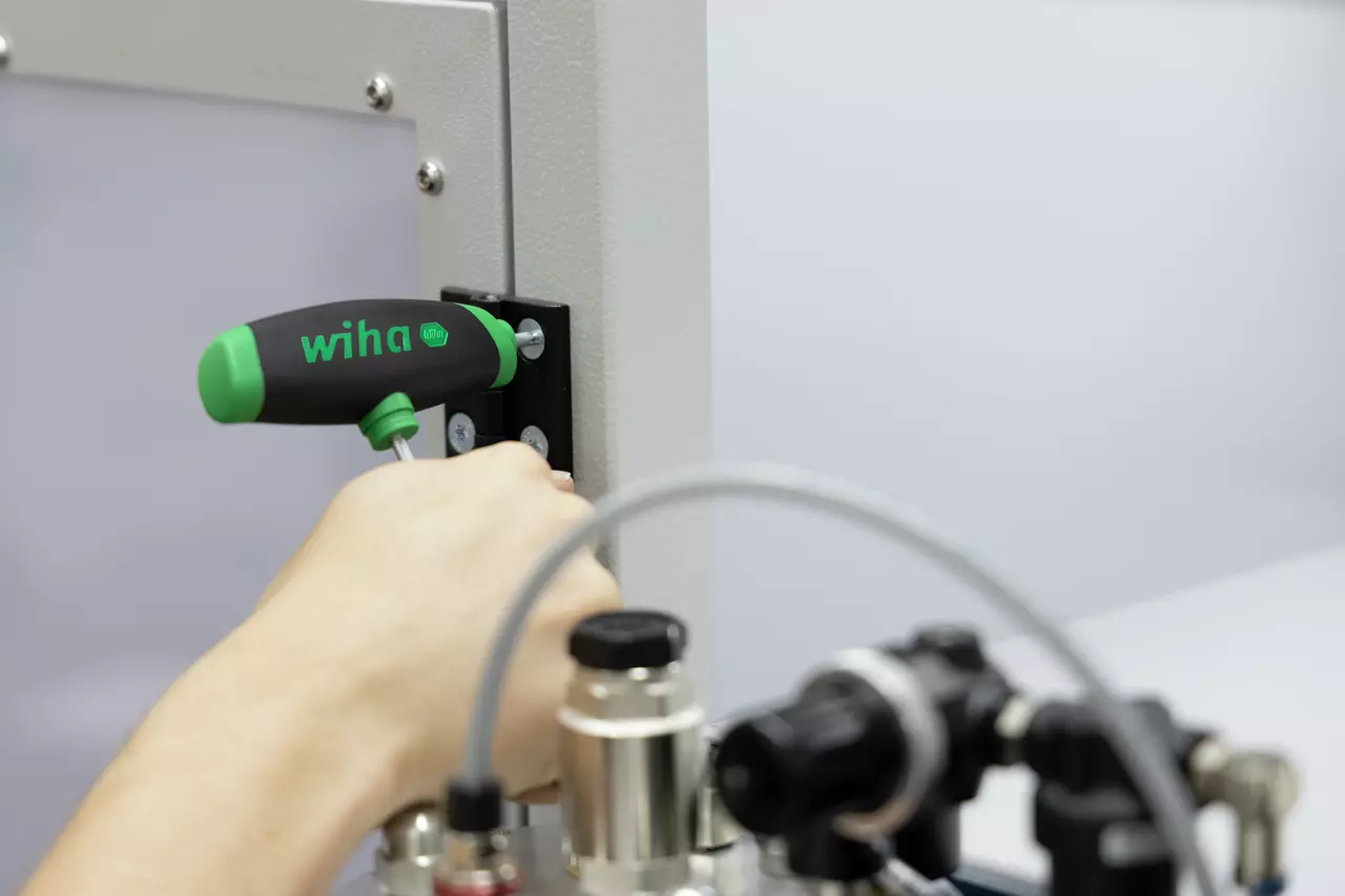 Person using a green and black T-handle tool on a metal surface