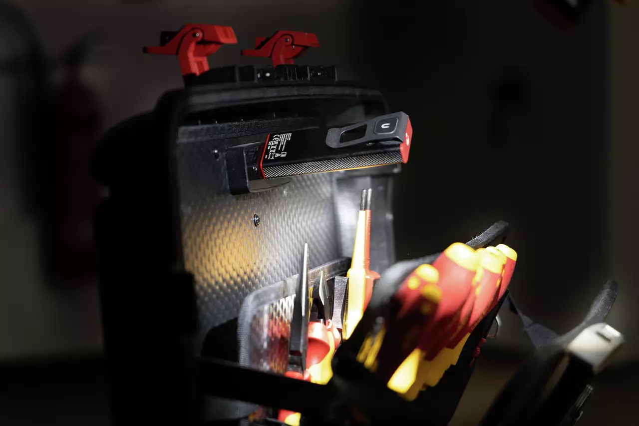 Werkzeugtasche mit magnetischer Handlampe und verschiedenen Handwerkzeugen, darunter Schraubendreher, in schwach beleuchteter Umgebung.