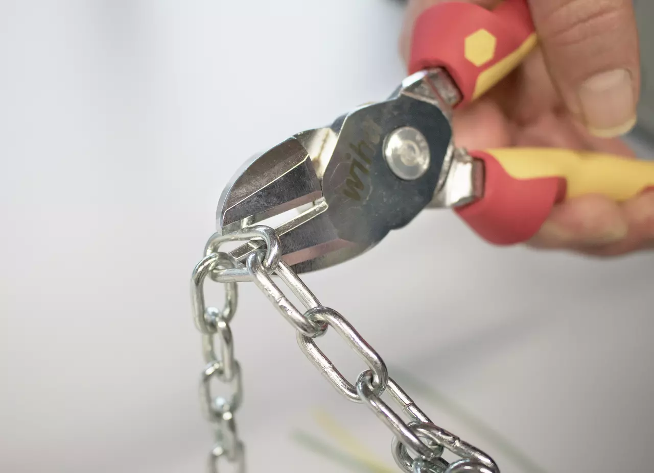 Diagonal cutters cutting a metal chain, held by a person.