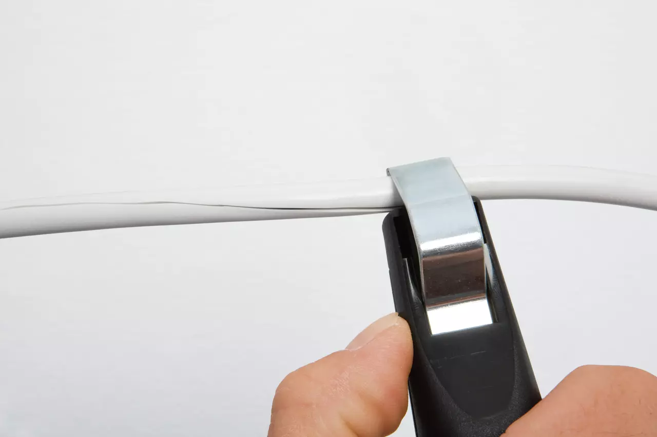 Hand using a cable stripping tool on a white wire.