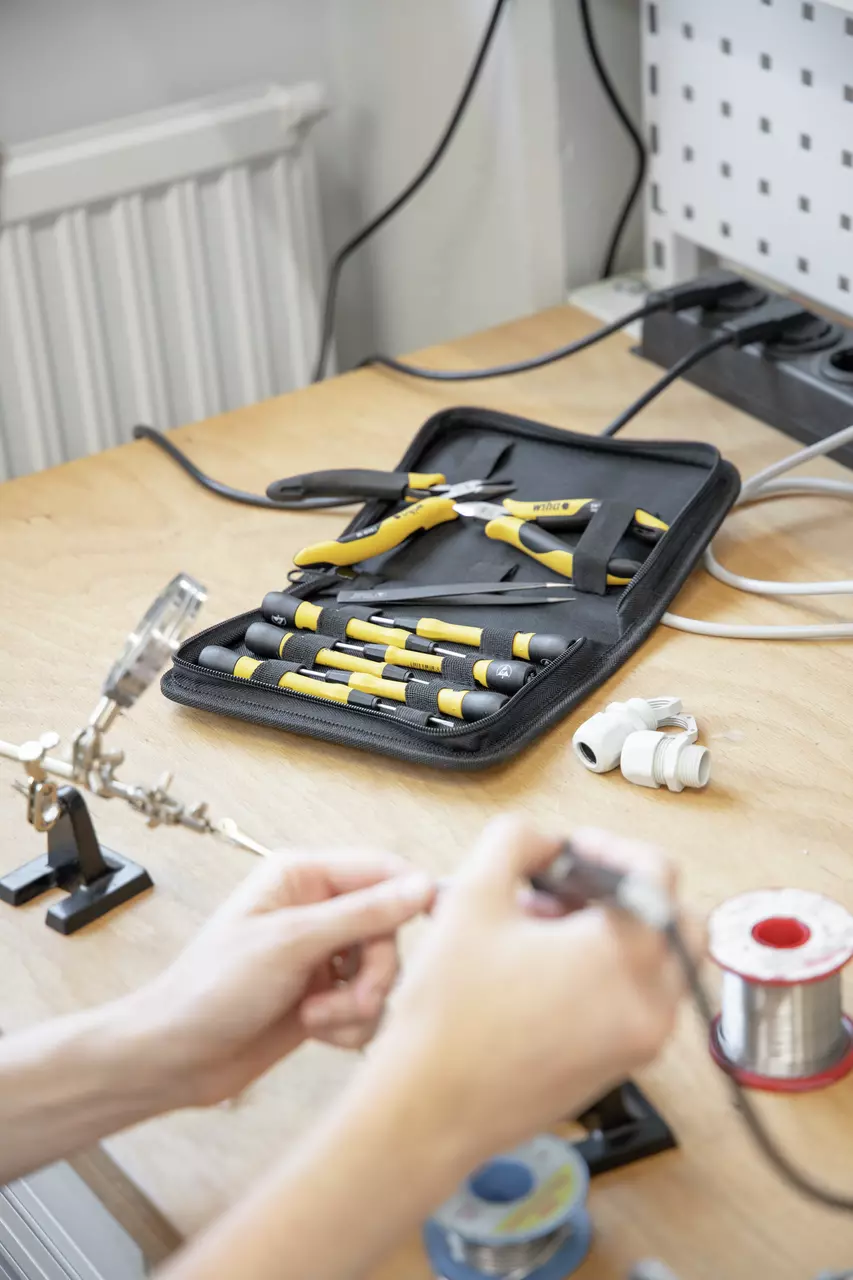 Tool set in yellow-black case on workbench, person working on electronics