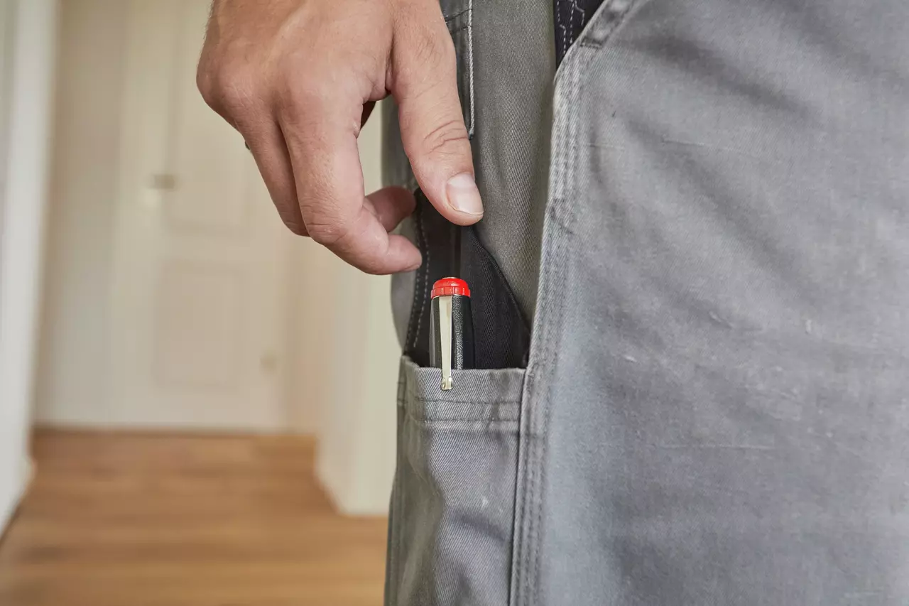 A person placing a voltage tester with a red cap into a pocket of gray pants.