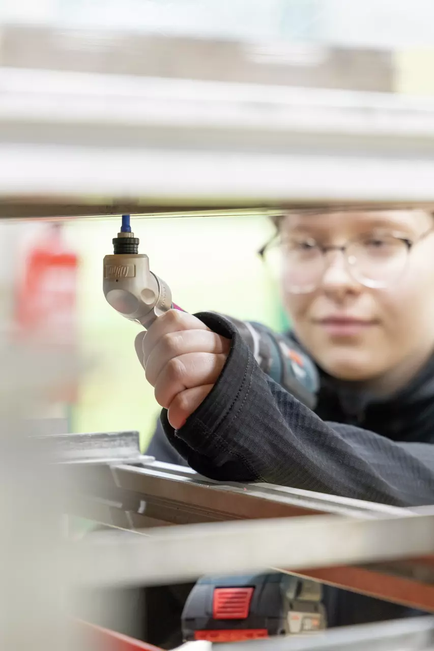 A person uses an electric screwdriver to work on a metal structure.