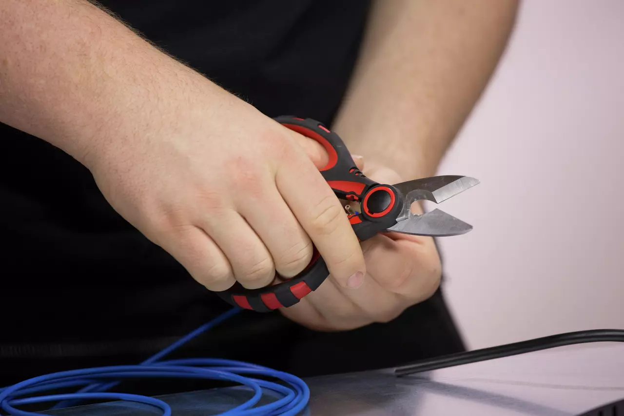 En person bruger rød-sorte elektriker saks til at klippe et blåt kabel.
