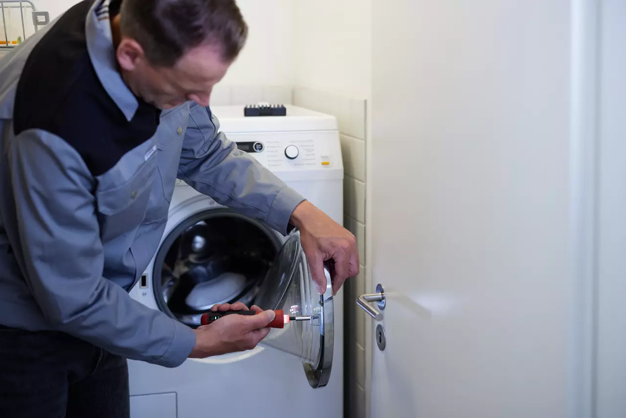 Person repairing washing machine door with electric screwdriver.