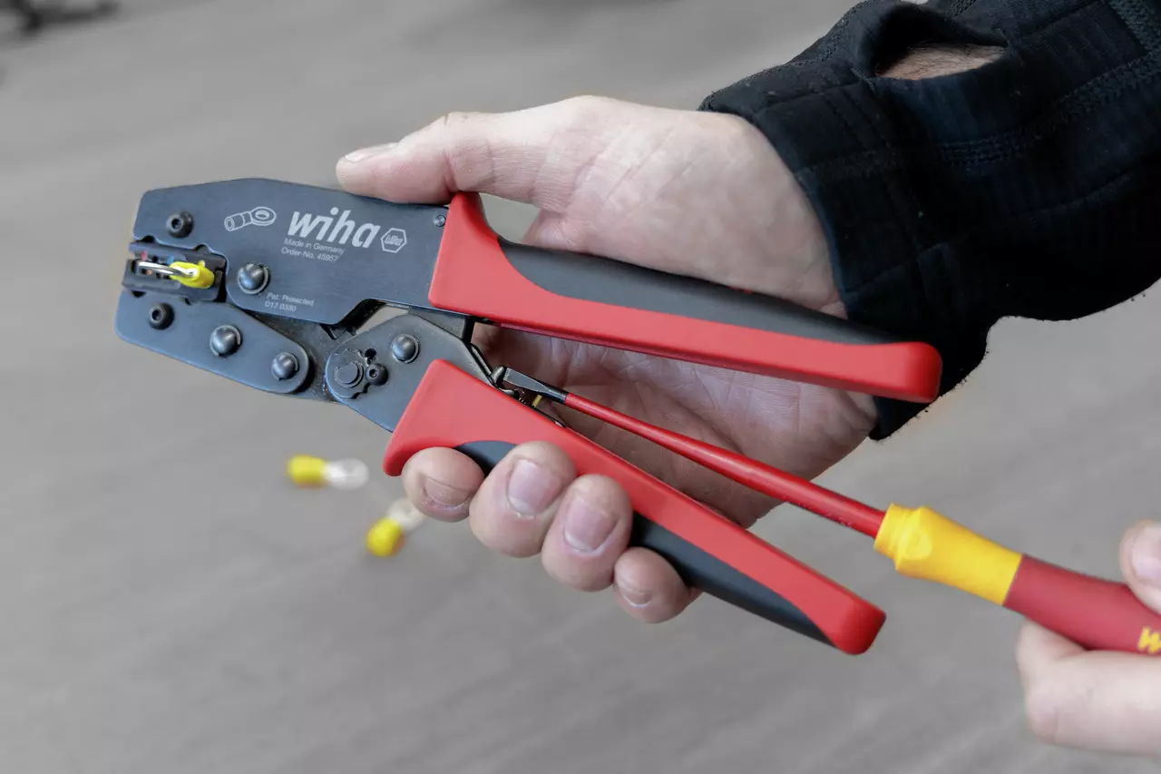 A person using a crimping tool with red and black handles to secure a yellow connector.
