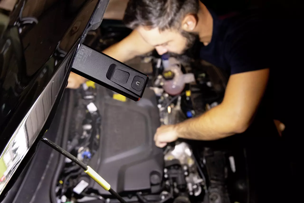 Ein Mann arbeitet unter einer Autohube mit einer schwarzen magnetischen Handlampe an der Haube.