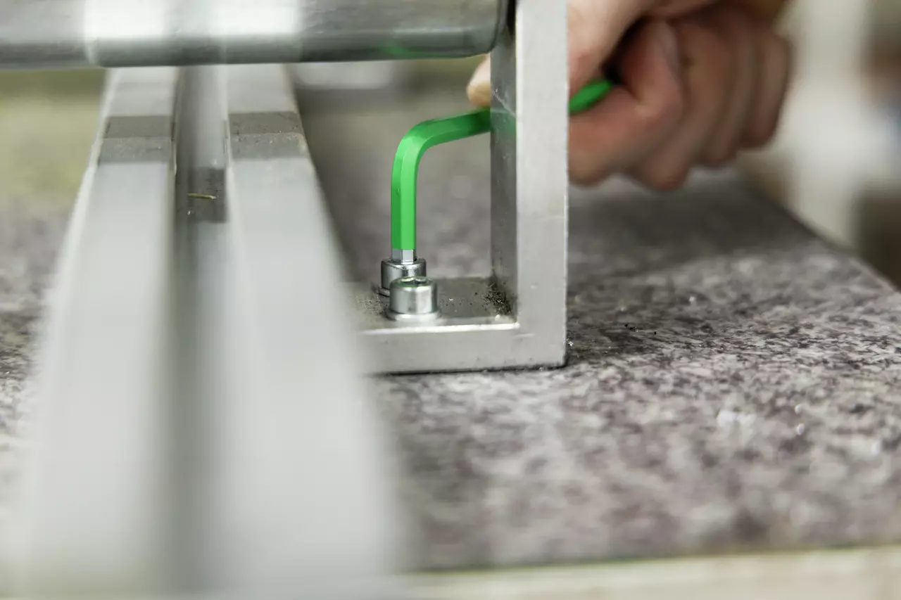 A hand using a green L-shaped key to tighten a bolt on a metal frame.