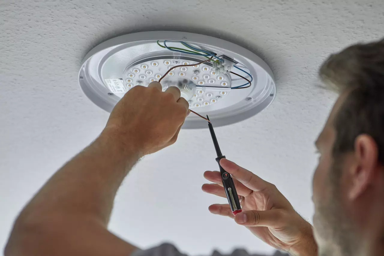 Person using voltage tester on ceiling light wiring.
