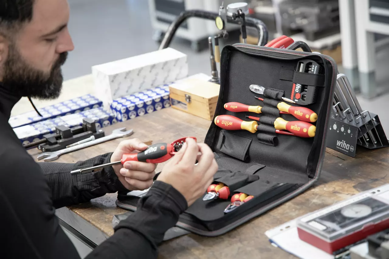 A person examining a tool set with red and yellow insulated screwdrivers on a workbench.