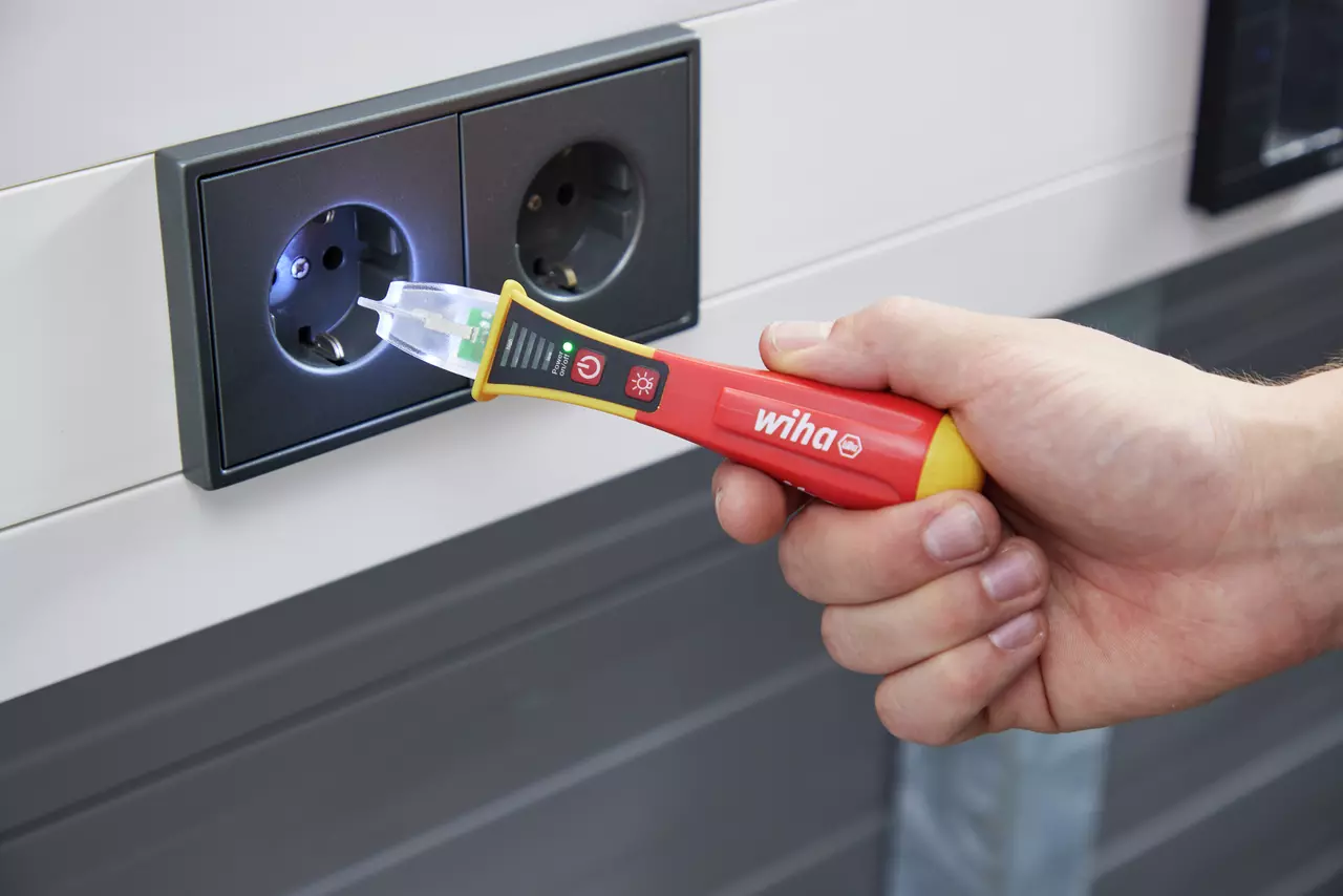 Hand holding a non-contact voltage detector near a power socket.