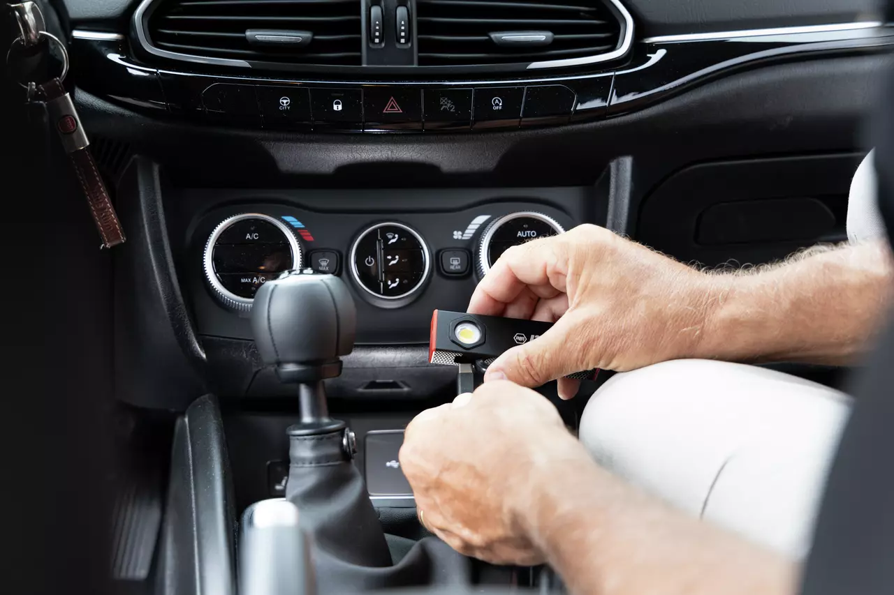 Person charging a small flashlight in a car's USB port, dashboard visible.