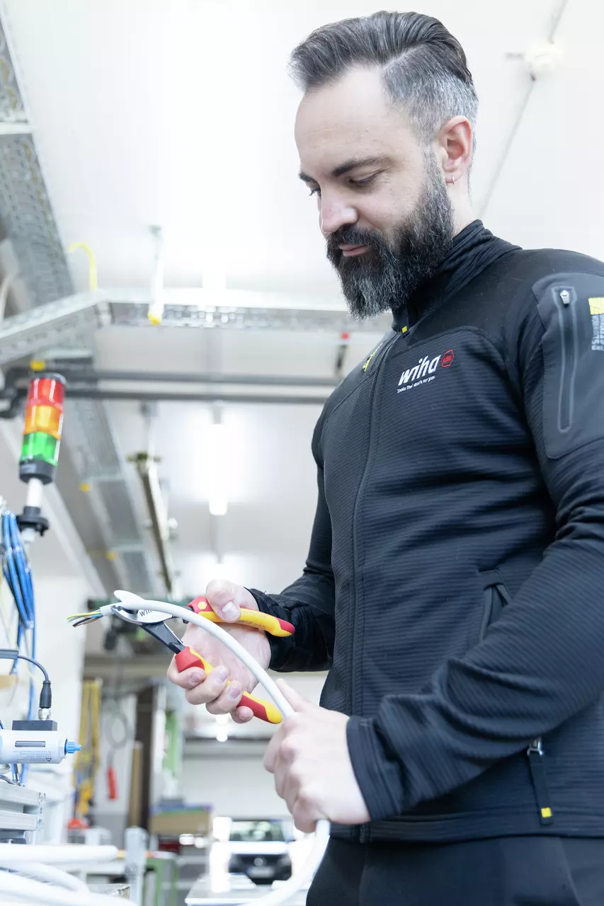 A person using an electric cable cutter on a thick cable in a workshop.