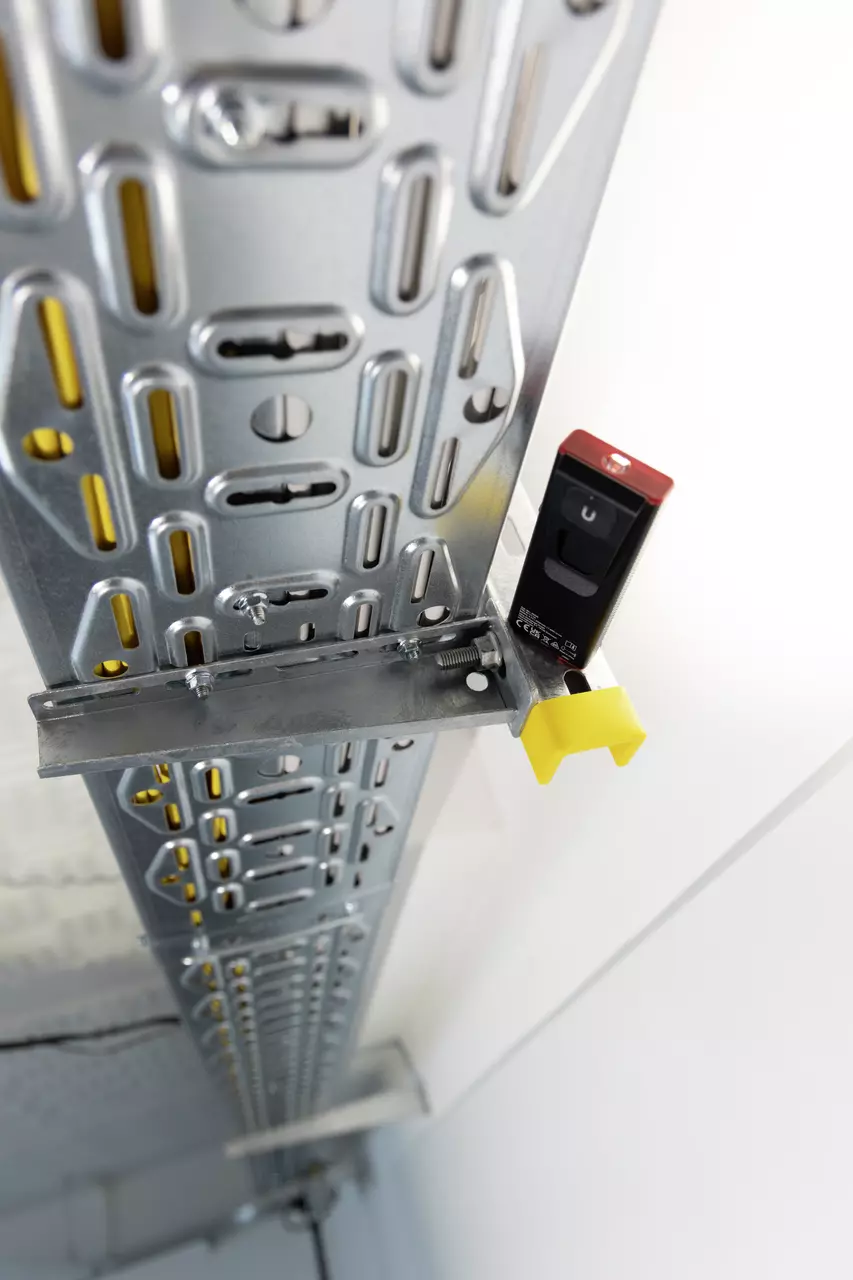 Metallschiene mit montiertem Sensor und gelber Halterung an einer Wand