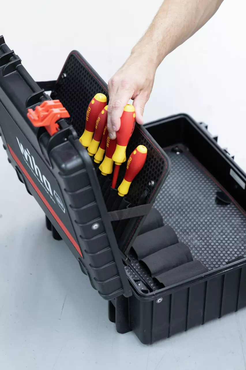Person placing screwdrivers in an open black toolbox.