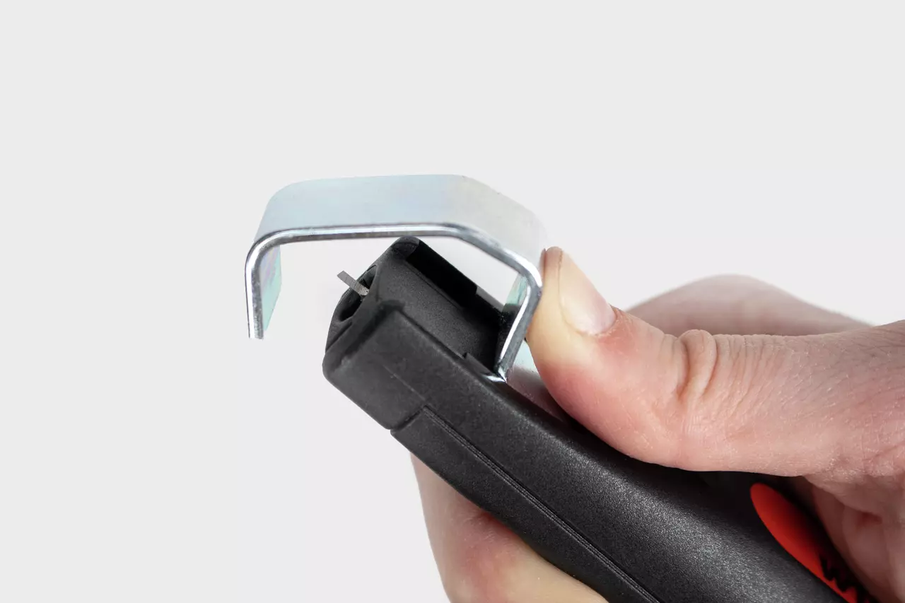 Wire stripping tool with a metal hook and black handle held by a hand.