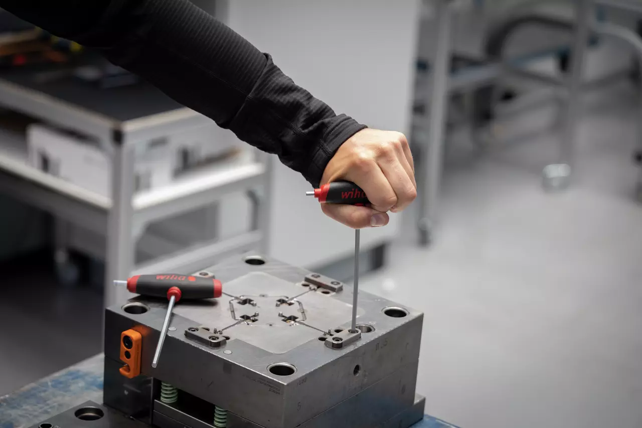 A person uses a hex key with a red and black handle on a metal fixture.