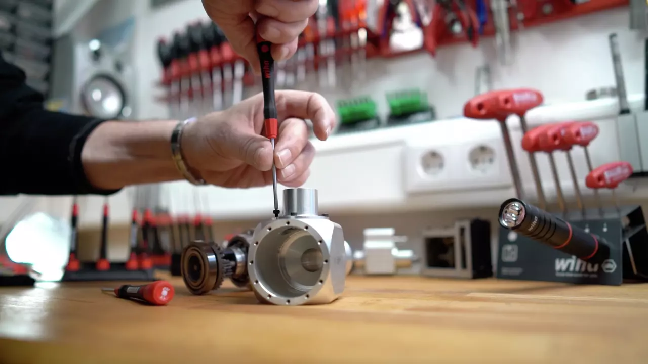 A person uses a precision screwdriver on a metal part in a workshop.