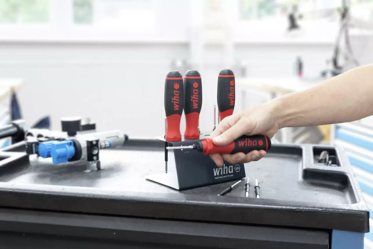 Hand holding red and black electric screwdriver from a set on a workbench.