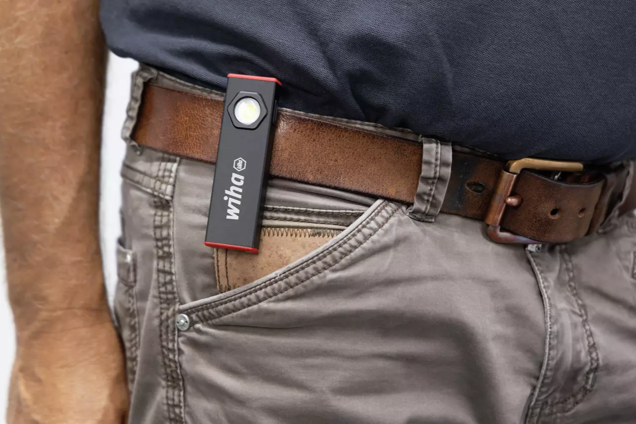 A person with a small flashlight clipped to a brown belt on beige pants.