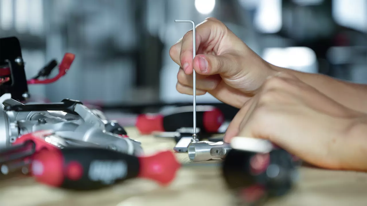 A person uses an L-shaped hex key on a small metal object, surrounded by tools.