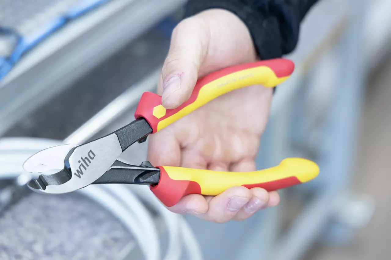 A person holding red and yellow insulated cable cutters, with metallic jaws, near cables.