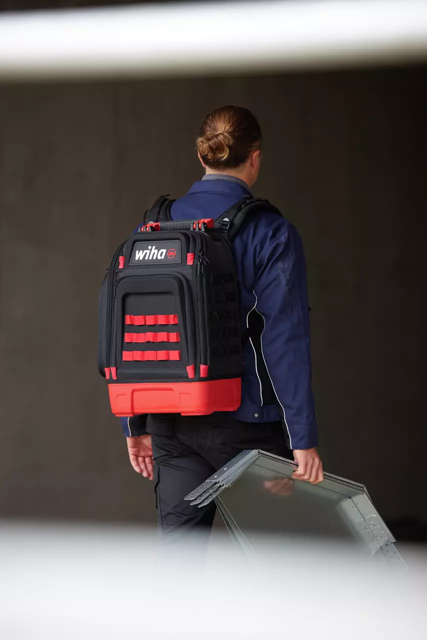 Person carrying a black and red backpack and a metal bracket indoors.