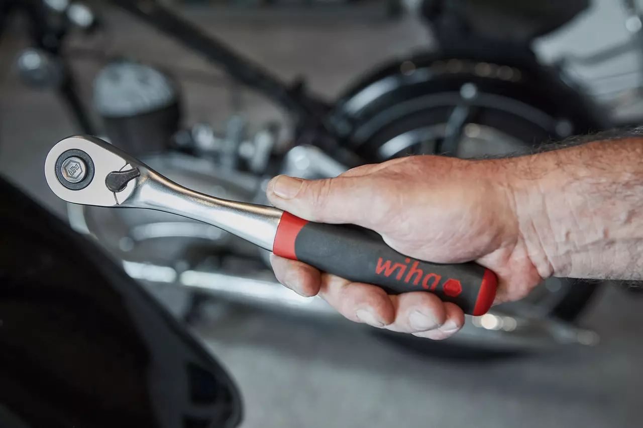 A hand holding a reversible ratchet with a black and red handle.