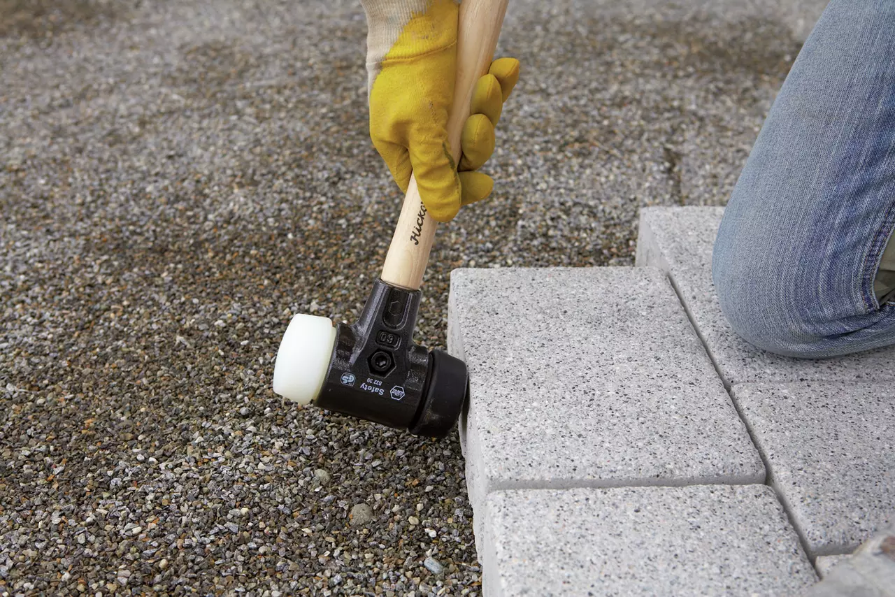 A person using a rubber mallet to adjust paving stones on gravel ground.